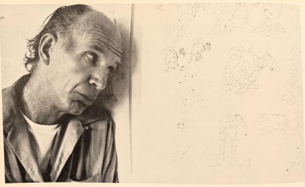 A man stands next to a wall, looking at drawings on it.
