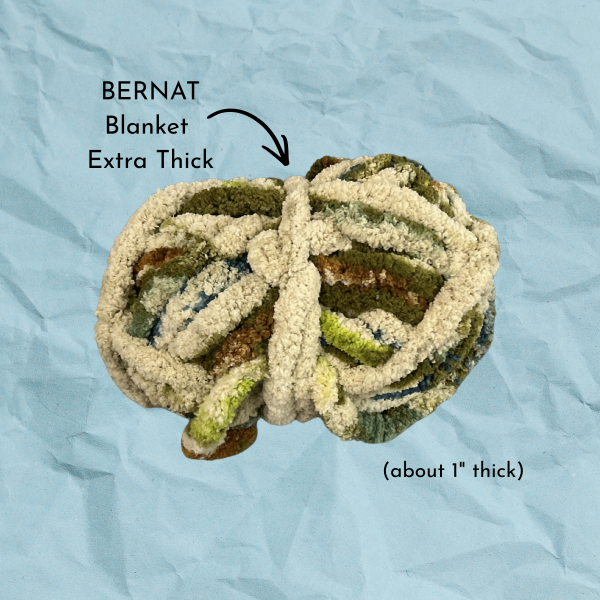 Blue paper texture background with multicolored yarn, text reading "BERNAT Blanket Extra Thick (about 1" thick)"