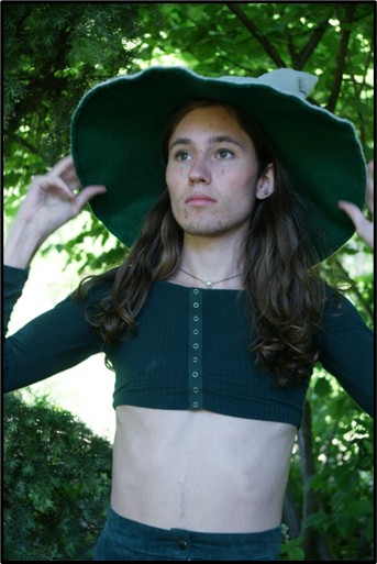 A person in a witch hat stands in a forest.