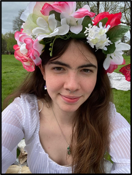 A person in a flower crown smiles at the camera in a field.